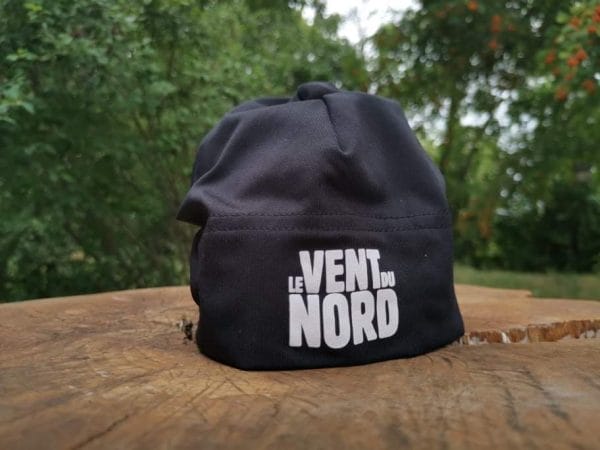 A black cap with the phrase "le vent du nord" printed on it, placed on a wooden surface outdoors.