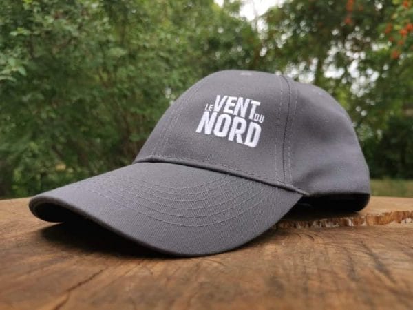 A gray baseball cap with the text "le vent du nord" printed on it, placed on a wooden surface outdoors.