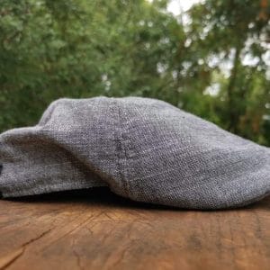 Gray flat cap placed on a wooden surface against a blurred natural background.